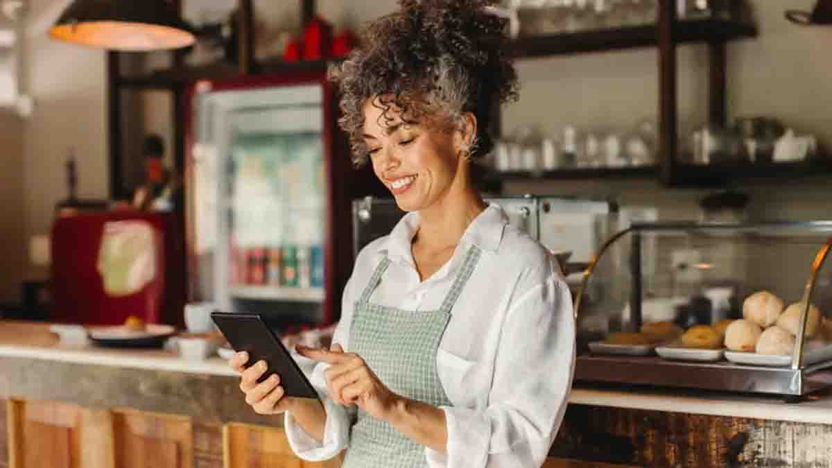 Woman in a cafe, wearing an apron, and using a tablet.
